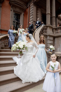 Bride and bridal party in blue gowns descend an exterior stone staircase carrying white bouquets
