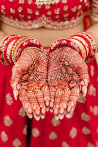 Indian bride displaying elaborately detailed mehndi on cupped palms adorned with red and gold bridal bangles against a vibrant red lehenga