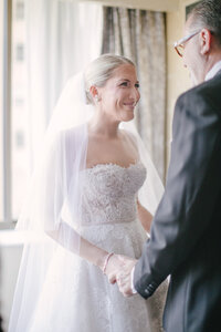 Bride smiles at her father holding his hand before the ceremony in a hotel room