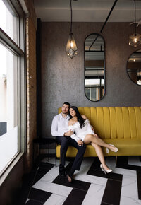 Couple cuddling on a mustard velvet couch during an engagement session by Angie Rich Photography, a San Antonio engagement photographer.