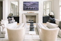 Bright white living room with sofas, boucle chairs, striped rug, stone fireplace, and moody horse artwork, creating an elegant, cozy atmosphere.
