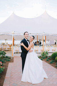Bride and groom pose together in front of a white reception tent