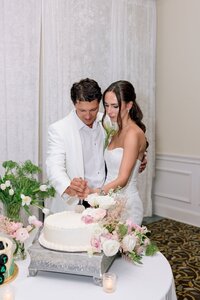 Bride and groom tenderly cut their white floral-adorned wedding cake together in an elegant ballroom reception