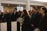 Emotional bridesmaid wiping tears while holding baby's breath bouquet during intimate church wedding ceremony