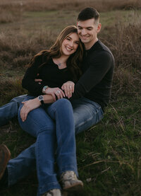 Smiling engaged couple embracing in an open field during golden hour portraits by Angie Rich Photography in San Antonio.