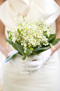 Close-up of a lily of the valley bouquet held in white gloved hands