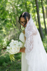 bride holding bouquet of flowers looking alongside her veil