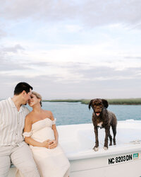 A couple sitting on their boat with their dog in the backdrop during their maternity photography session at Wrightsville Beach, North Carolina