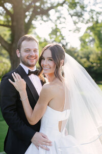 Bride and groom smile together in a close portrait backlit by golden sunlight through trees