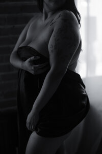Plus-size woman wrapped in black sheets while standing during a plus size boudoir Dallas boudoir session.