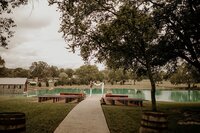 wedding ceremony at Steel Magnolia Barn with wooden benches , an arbor decorated with flowers and drapery and a lake
