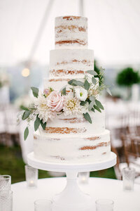 Five tier wedding cake decorated with blush roses and white dahlias under a reception tent