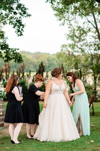 Wedding planners with Weddings & Events by Raina assist the bride with bustling her wedding dress