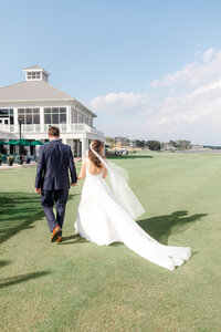 Bride and groom walking across the waterfront lawn at Rehoboth Beach Country Club on their wedding day in coastal Delaware.