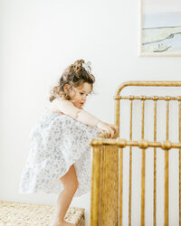 A toddler girl smiling and climbing into her crib during an in home family photography session in Wilmington, North Carolina