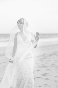 Black-and-white bridal portrait on the beach in Bethany Beach, Delaware, with her veil blowing softly in the ocean breeze.