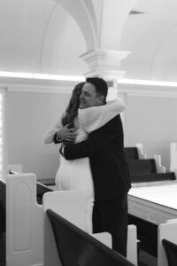 A bride in a white gown shares a heartfelt embrace with her father amid the arched interior of Liberty University Chapel