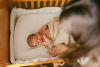 A mother tucks her newborn baby into her crib during their at home newborn photos in houston tx