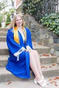 A classic photo taken by Studio Roscher of a happy high school female graduate in her blue graduation gown in Alexandria, VA