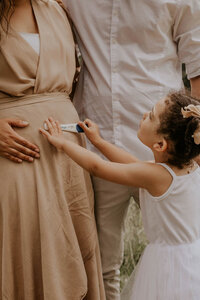 family pregnancy announcement with little girl holding positive pregnancy test against moms belly