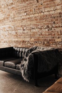 Black leather tufted couch with faux fur throw in front of exposed brick wall. warm, stylish corner of Love, Kay Collective’s boudoir studio in Tampa, Florida.