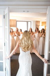Bride opens double doors to reveal her dress to bridesmaids reacting with joy
