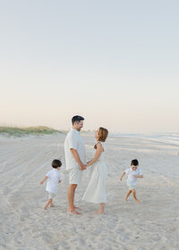 A mom, dad, and two toddler boys playing and laughing on the beach during their sunset family photography session at Wrightsville Beach, North Carolina