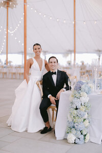 Bride and groom smile together at a table lined with blue and white hydrangea flowers
