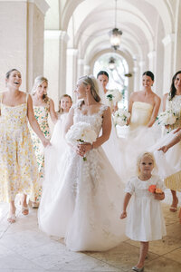 Bride walks through an arched courtyard with bridesmaids in yellow floral dresses