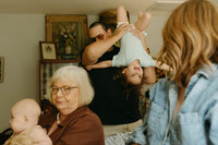A father holds his toddler upside down and the grandmother gazes at me disapprovingly during their at home extended family photo session in houston texas