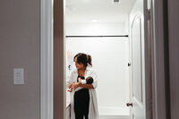 A mother holds her newborn while washing her hands off in the restroom during their at home newborn photos in houston tx