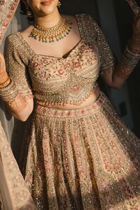 South Asian bride smiling in an ornate gold embroidered lehenga with floral mehndi and layered gold jewelry at her Norfolk wedding