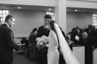 Smiling groom holds bride's hands at the altar as an officiant reads vows during an intimate chapel ceremony