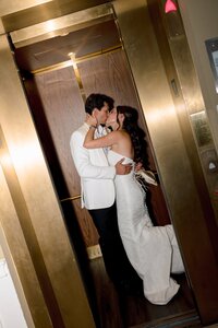 Bride and groom share a passionate kiss inside a gleaming gold elevator at Belmont Country Club, romantic and candid