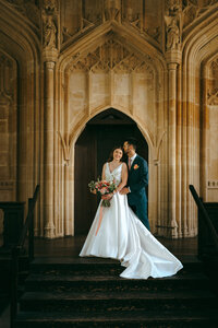 Bride and groom standing together in a grand stone archway at an Oxford college venue