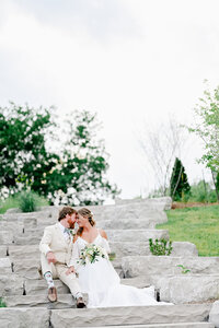 A bride and groom embracing each other while sitting on steps taking their wedding portraits.