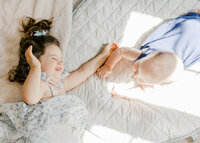 A toddler girl and her baby brother laying on the floor smiling during an in home family photography session in Wilmington, North Carolina