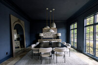 Ohio dark-blue dining room with a black table, cream chairs, pendant lights, marble fireplace, and tall windows; moody yet inviting.