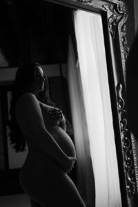 A black and white maternity photo of a beautiful mama holding her baby bump in the mirror during a Dallas maternity boudoir session.