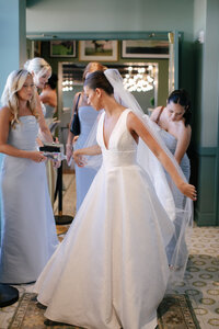 Bridesmaids help the bride into her v-neck wedding gown before the ceremony