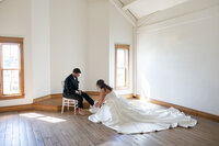 bride helping groom put on his shoes, preparing for their wedding reception in ohio