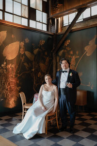 Bride and groom pose beside a hand painted botanical mural on a checkered tile floor
