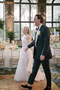 Bride and groom walk laughing into the palm filled reception ballroom at The Breakers Palm Beach