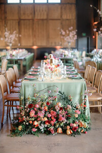 Long reception table features an abundant floral runner in coral pink and burgundy tones