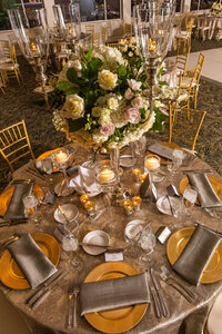 Elegant wedding reception table with gold chargers, silver linens, white floral centerpiece and candlelight.