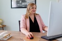 A classic professional portrait taken by Studio Roscher of a female professional smiling while working on her computer in her home office