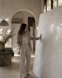 Designer viewing a polished Calacatta quartz slab with soft gray veining in a contemporary stone showroom.
