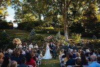 Wedding ceremony in the woods with the bride in a long lace dress and veil and the groom wearing a dark gray suit