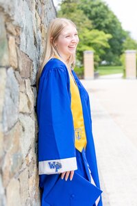 A classic photo taken by Studio Roscher of a happy high school female graduate in her blue gown and yellow sash in Alexandria, VA
