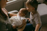 A young boy kisses his baby sisters head during their at home newborn photos in houston tx
